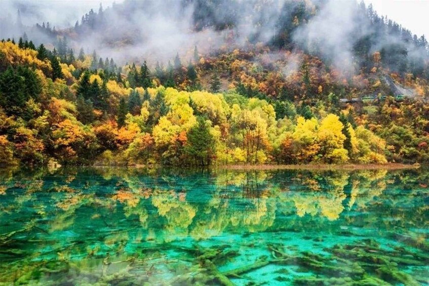 A clear lake reflecting colorful autumn trees and a misty mountain in the background. 5