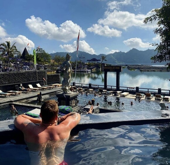 A man relaxing in a hot spring pool with a statue and a dock in the background. 5