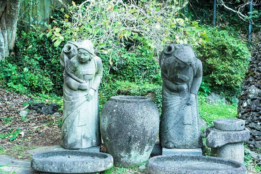 Stone statues of a woman and a child in a garden with greenery and stone structures. 2