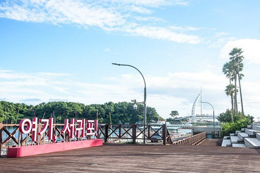 A wooden boardwalk with a sign, palm trees, and a bridge in the background. 5