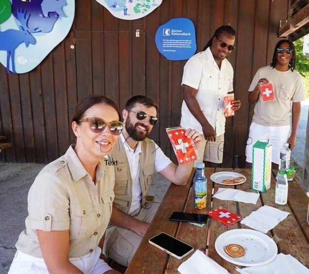 A group of people at a wooden table with Swiss flags, a water bottle, and a Swiss flag box. 3