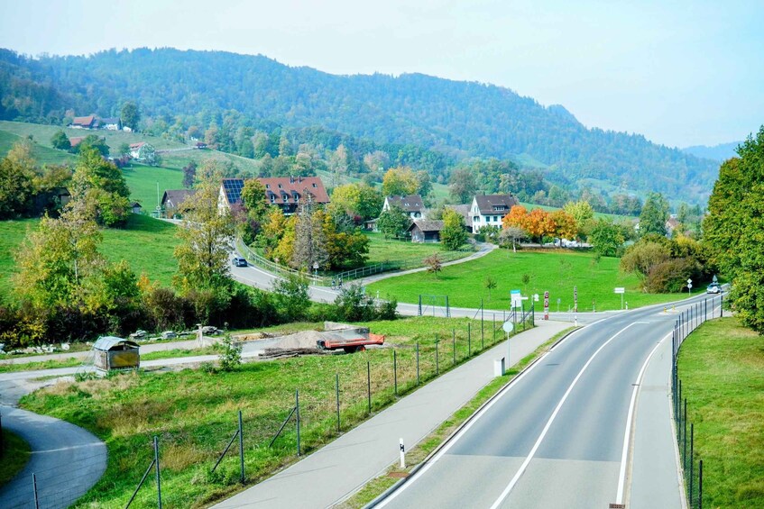 A rural road curving through a valley with houses and trees on either side. 2