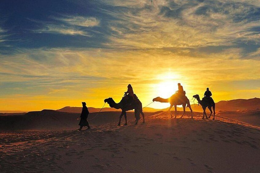 A desert landscape with three camels and riders silhouetted against a sunset. 4