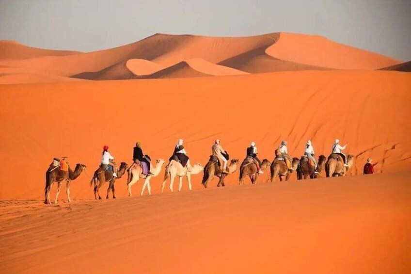 A group of people riding camels across a desert landscape with sand dunes in the background. 1