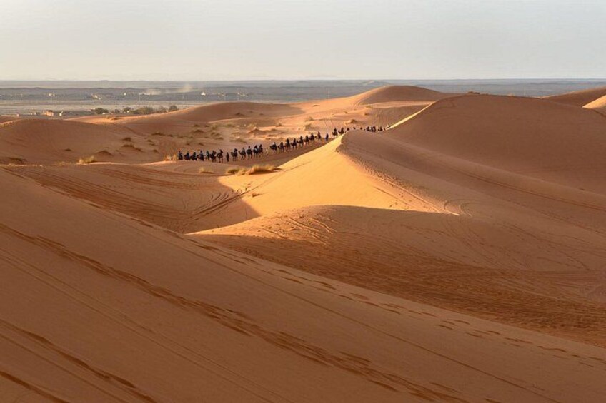 A group of people riding camels across a desert landscape with sand dunes. 3