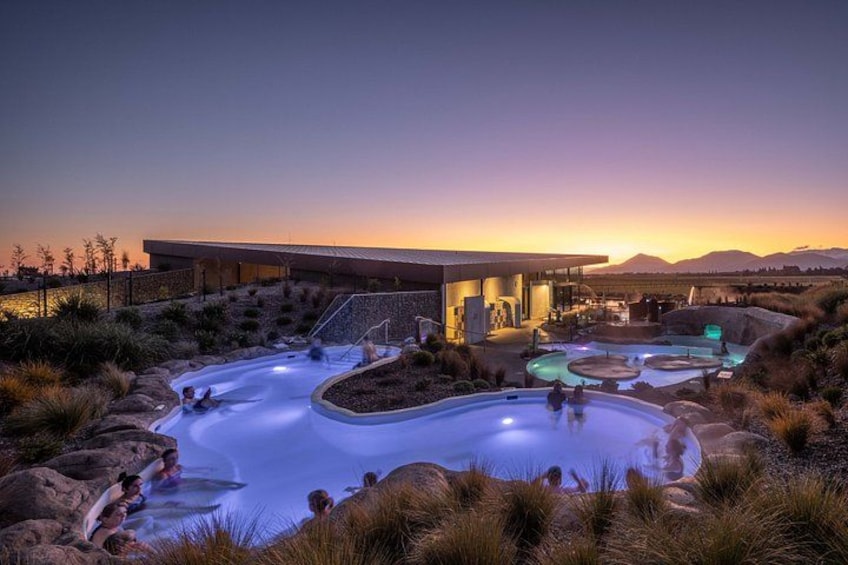 A hot spring resort with multiple pools and a modern building at sunset. 3