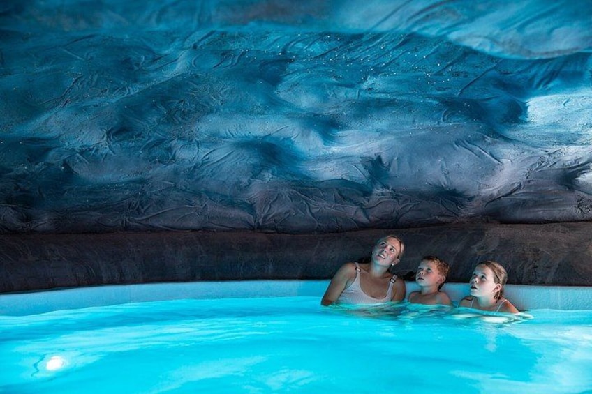 An indoor swimming pool with a blue hue and a ceiling resembling an ice cave. 4