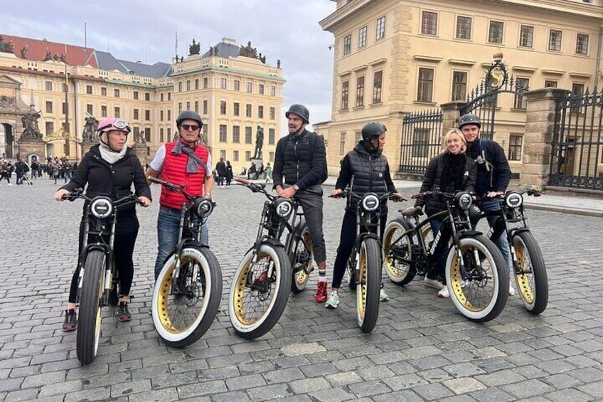 A group of people on bicycles in a cobblestone square with historic buildings in the background. 2