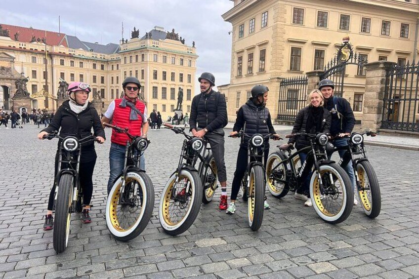 A group of people with bicycles in a cobblestone square with historic buildings in the background. 2