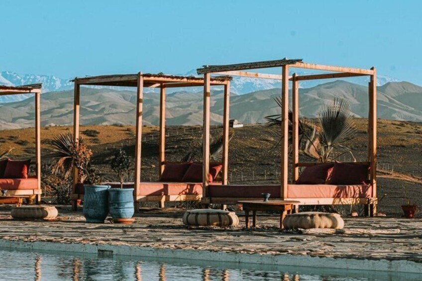 A rustic outdoor seating area with wooden structures and red cushions, set against a mountainous backdrop. 5