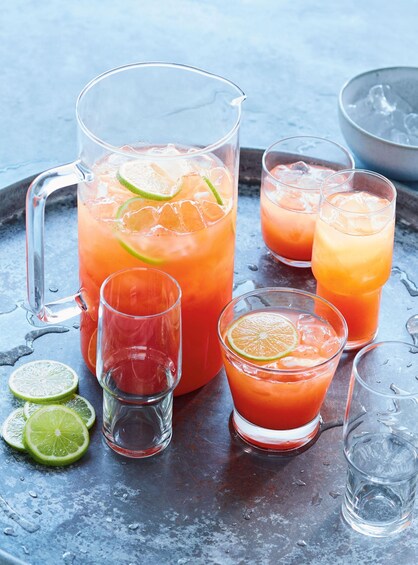 A pitcher and glasses of a red beverage with lime slices, ice cubes, and a metal tray. 2