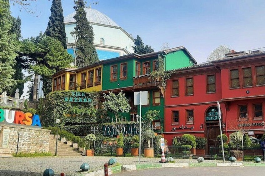 A street with colorful buildings, a sign reading 'BURSA,' and a dome structure in the background. 1