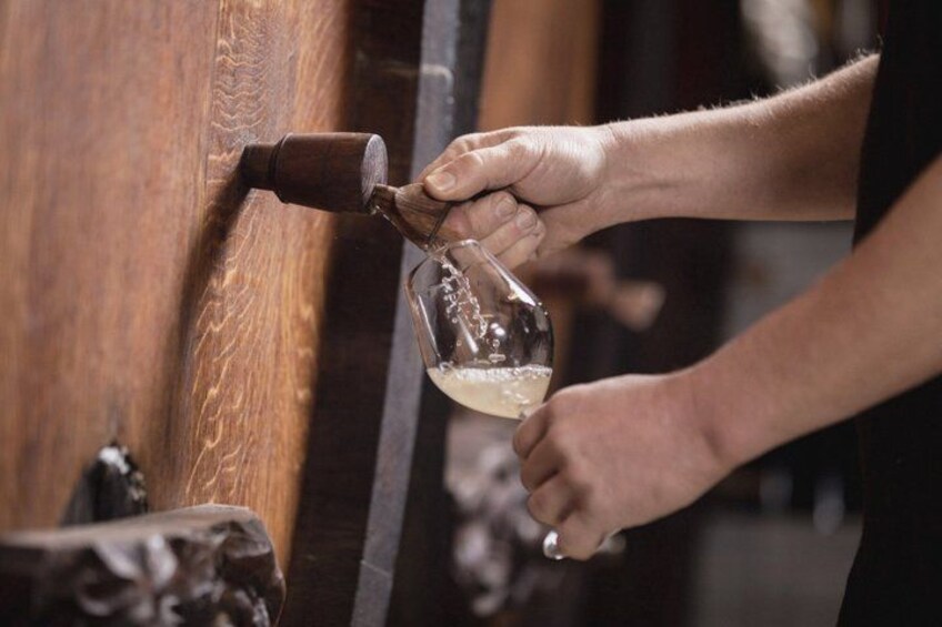 A person pouring a liquid from a glass into a wooden container. 2