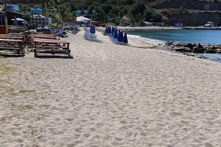 A sandy beach with wooden benches, blue umbrellas, and a rocky shoreline. 3