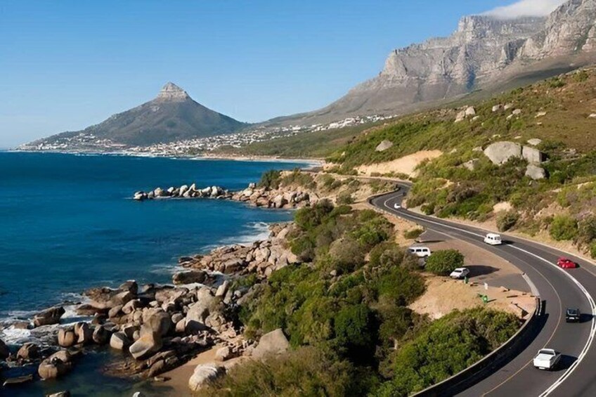A coastal road with vehicles, a mountain, and a beach. 3