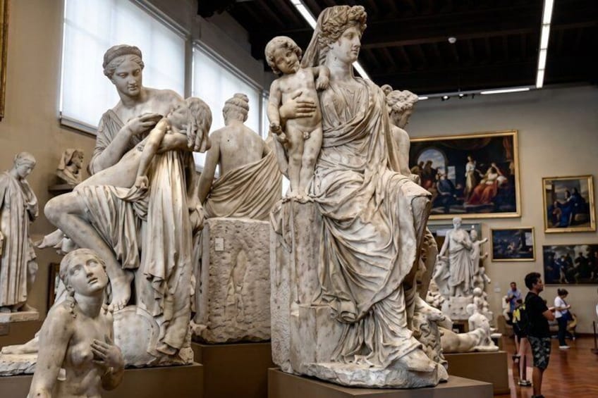 A marble sculpture of a woman holding a child, surrounded by other classical statues in a museum. 4