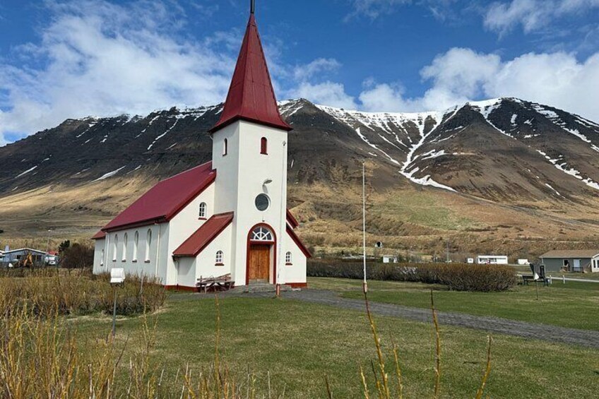 A white church with a red roof and a tall steeple, set against a backdrop of snow-capped mountains. 4