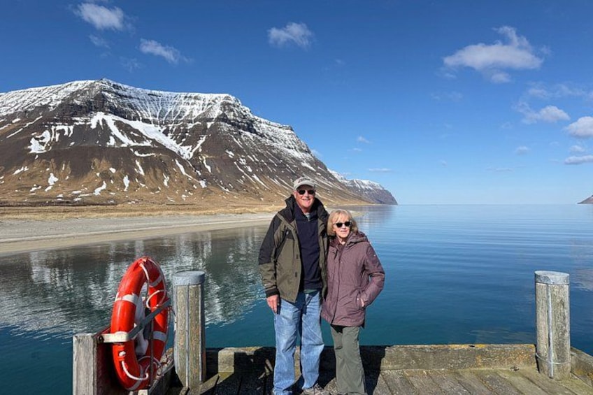 A wooden dock with a lifebuoy, a calm lake, and a snow-capped mountain in the background. 5