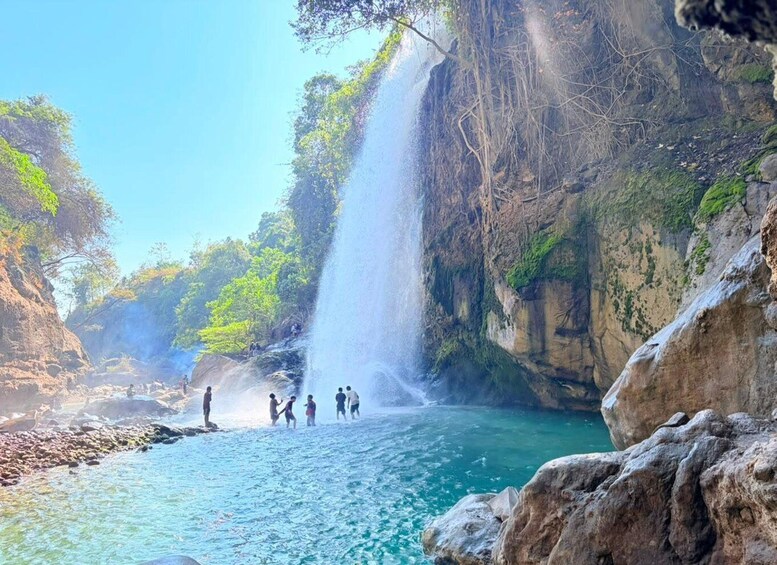 A waterfall cascading into a clear blue pool surrounded by rocky cliffs and greenery. 1