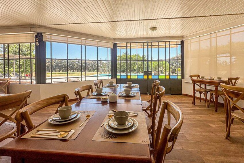 A dining area with wooden tables and chairs, large windows with a view of greenery and a building. 5