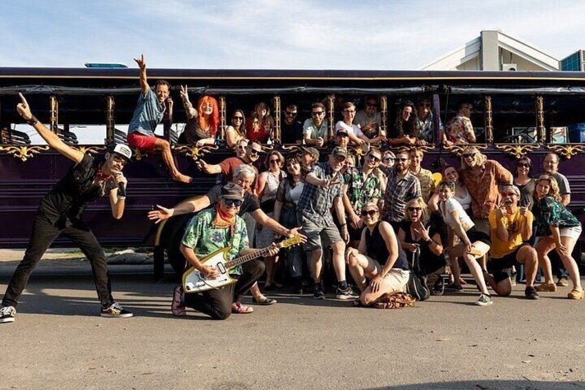 A group of people posing in front of a purple bus with a man playing an electric guitar. 3