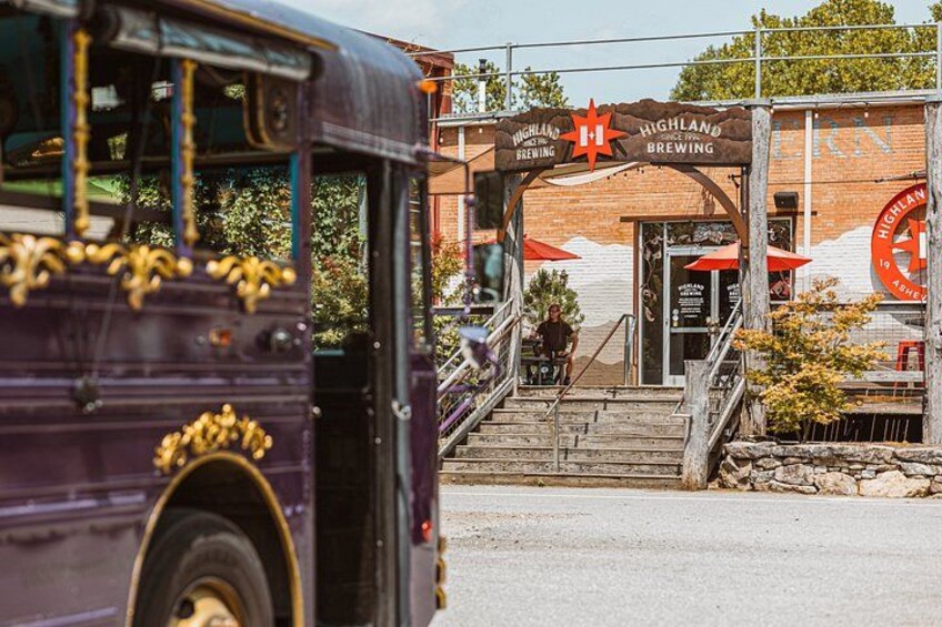 A purple bus parked in front of Highland Brewing, with a wooden staircase leading to the entrance. 2