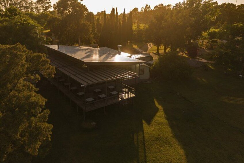 A large, open pavilion with a flat roof, surrounded by trees and grass. 2