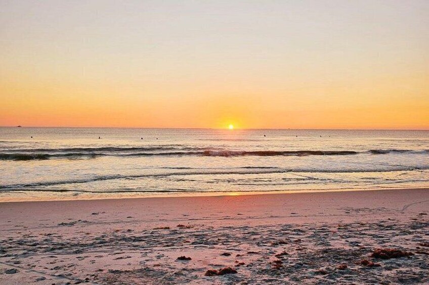 A beach at sunset with the sun near the horizon, waves on the shore, and a clear sky. 5