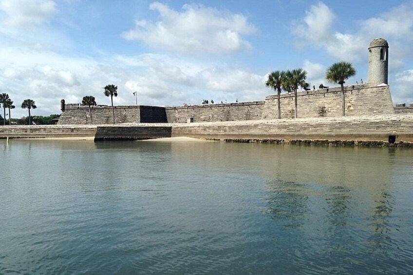 A fortified structure with a tower, palm trees, and calm water. 4