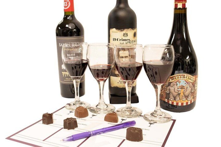 Three wine bottles, two wine glasses, and a tasting sheet with chocolate pieces. 2