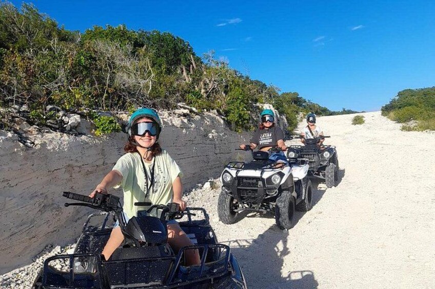 Two people riding ATVs on a sandy path with vegetation on the sides. 1