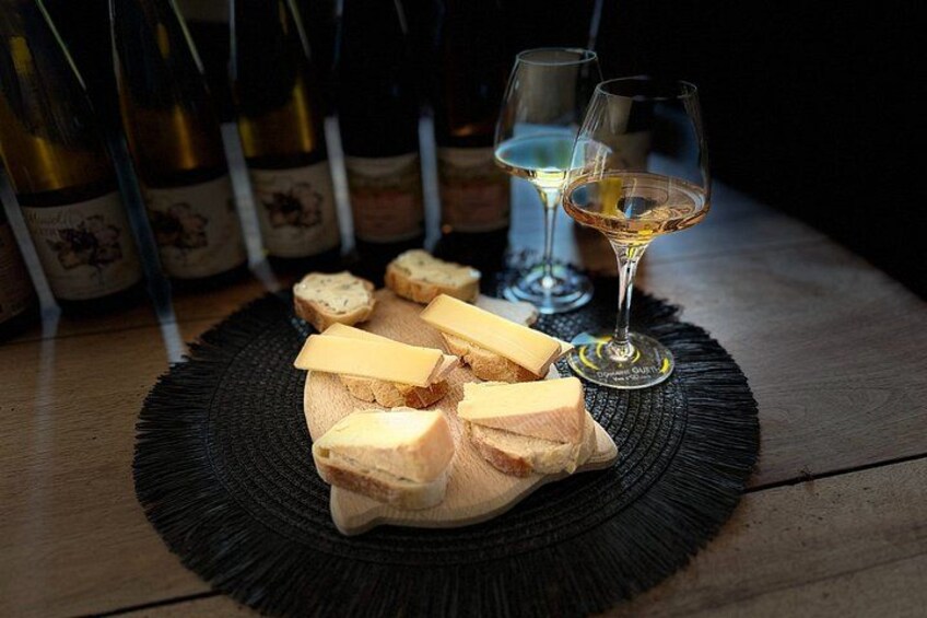 A round black placemat with cheese and wine glasses on a wooden table. 1