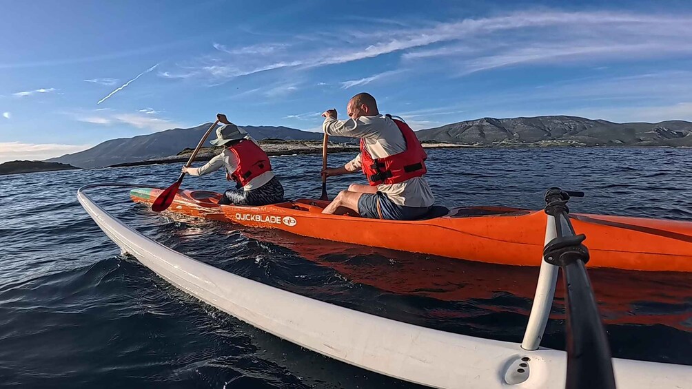 Two people kayaking in an orange kayak on calm water with mountains in the background. 5