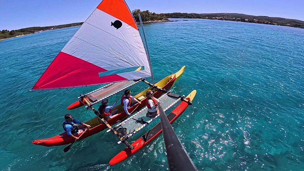 A sailboat with a red and white sail, two rowers in red life jackets, and a third person steering. 4