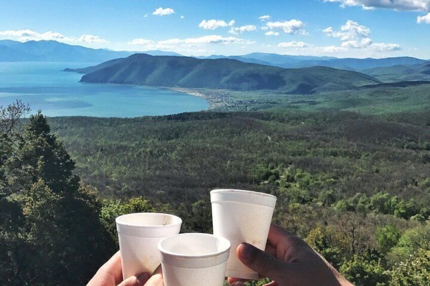 A hand holding three paper cups, overlooking a mountainous landscape with a body of water. 1