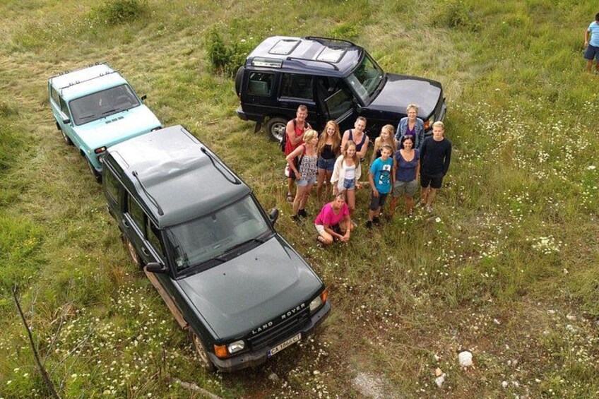 A group of people standing in a grassy field with two vehicles parked nearby. 2