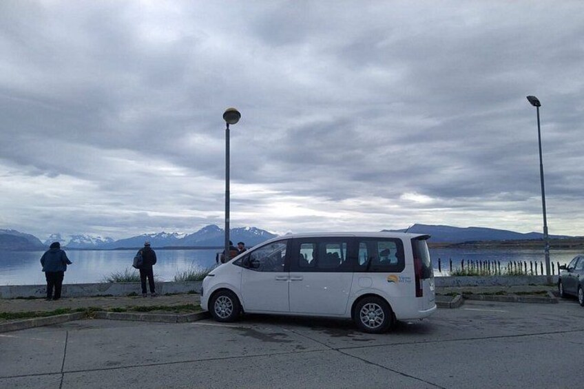 A white car parked on a paved area near a body of water with mountains in the background. 2