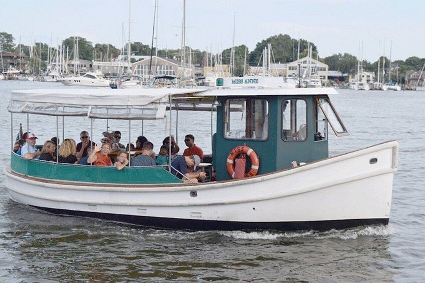 A boat with people on board, docked at a marina with other boats and buildings in the background. 1