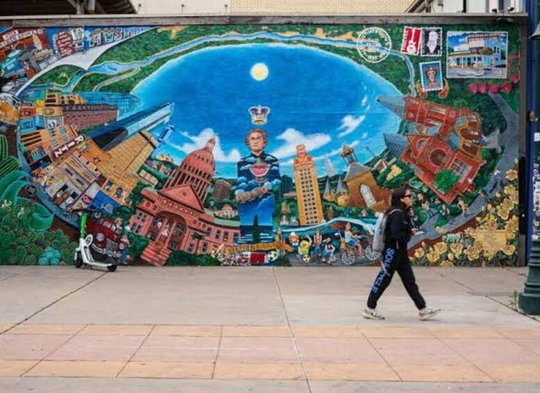 A mural with a cityscape, a large blue sky, and a person walking. 1