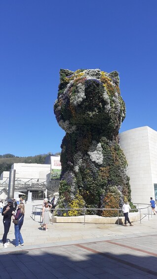 A large floral sculpture resembling a bear in an outdoor public space. 2
