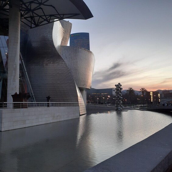 A modern architectural building with a reflective surface, a body of water, and a sunset sky. 1