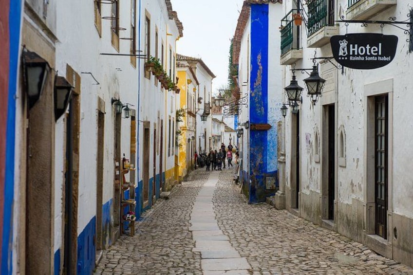 A cobblestone street lined with colorful buildings, a hotel sign, and a blue pillar. 3