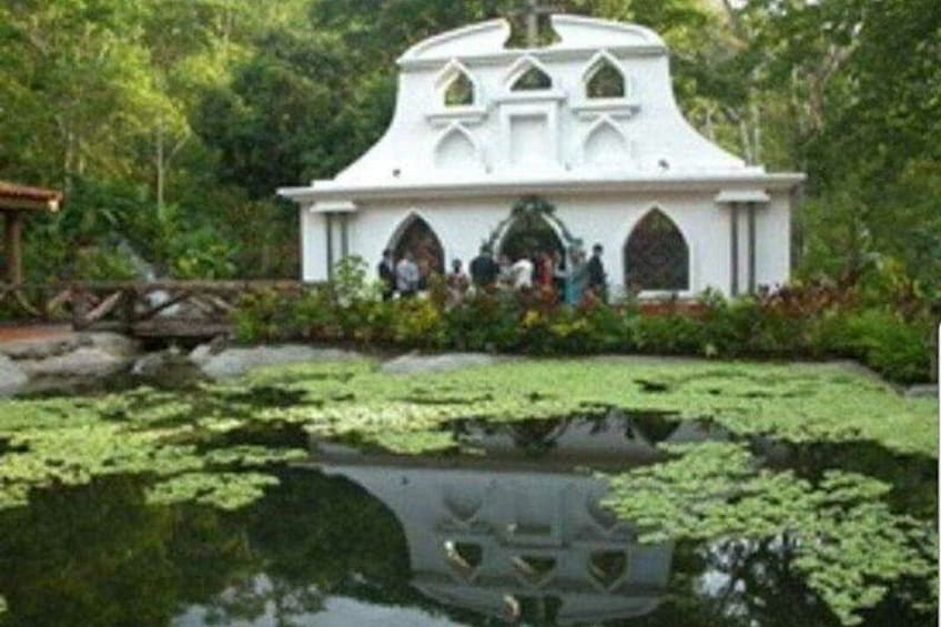 A white building with gothic architecture, surrounded by lush greenery and a pond with lily pads. 5