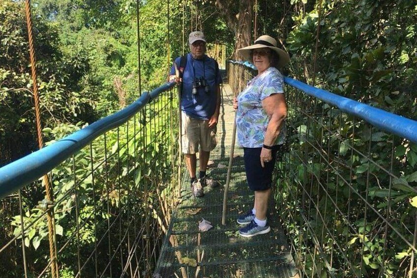 Two people walking on a suspension bridge surrounded by dense foliage. 4