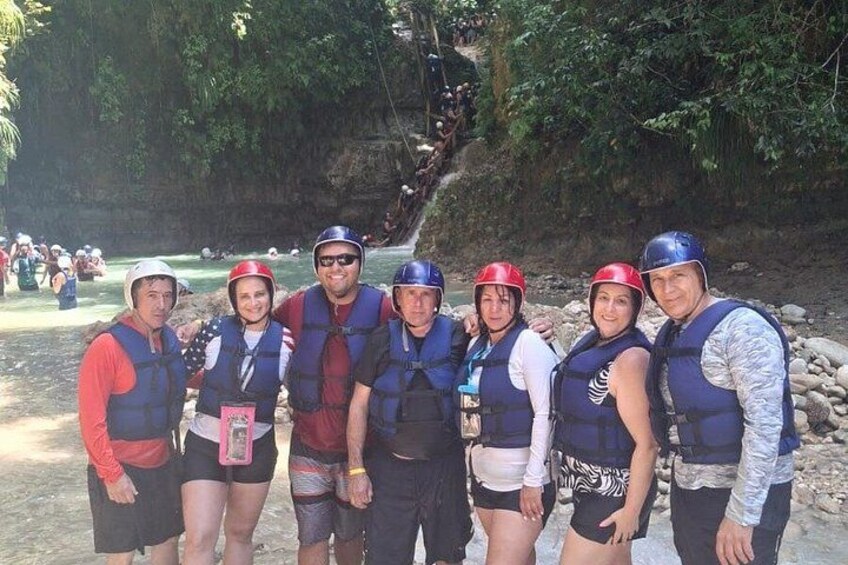 A group of people wearing life jackets and helmets, standing on a rocky shore with a river in the background. 4