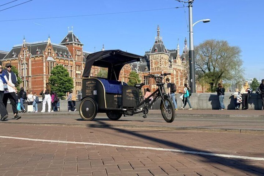 A street scene with a black and blue carriage, pedestrians, and historic buildings in the background. 1