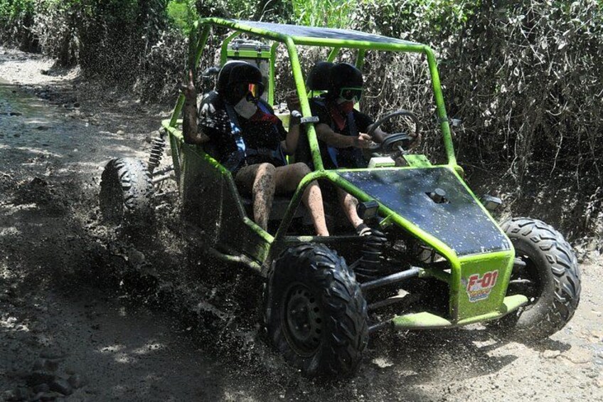 A green off-road vehicle with two occupants driving through a muddy terrain. 2
