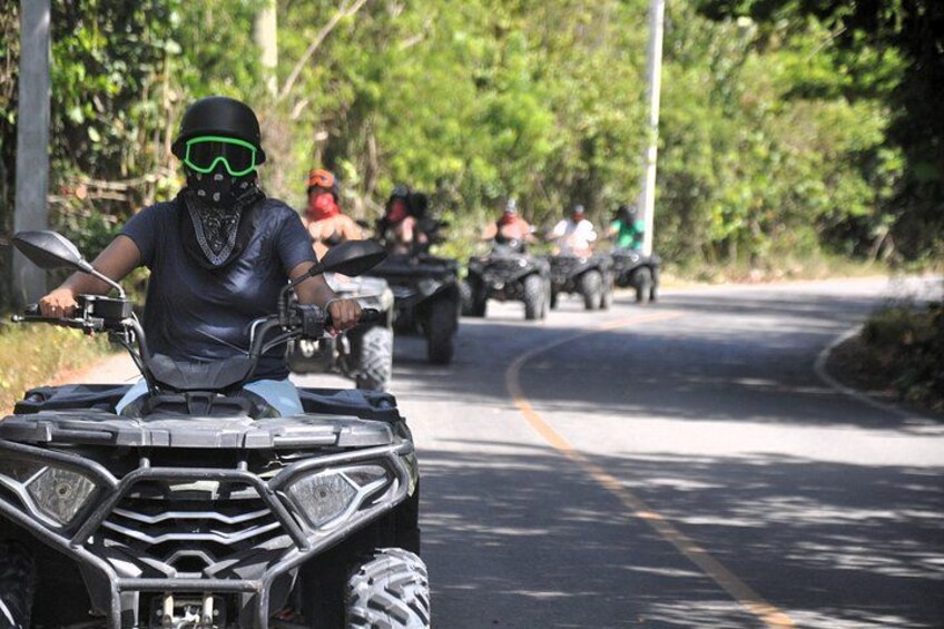 A person riding an ATV on a road surrounded by greenery. 4