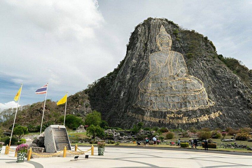 A large Buddha statue carved into a mountain, surrounded by flags and a paved area with benches. 4