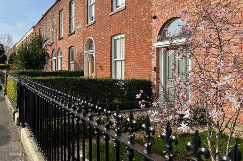 A brick house with a black iron fence and flowering trees. 1